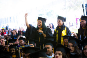 Girls wearing Commencement outfits cheer in the graduation tent. 