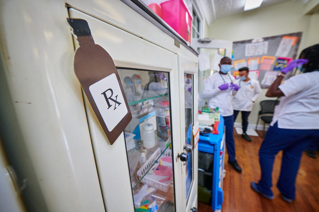 Health professions students gather in the background of the image, with a focus on a cutout on a cabinet, featuring the letters 'RX'.