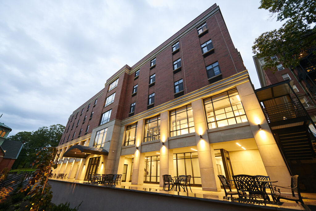 A close up view of the south side of Aquino Hall in the evening, with lights illuminating the exterior first and second floors.