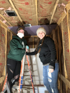 Two students smile while standing on a ladder. 