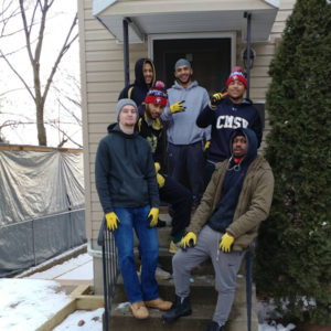 Members of the Men's Basketball team pose on the front steps of a house they are rebuilding. 