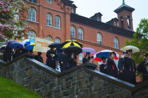 Graduates walk down the centennial steps holding umbrellas. 