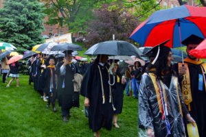 Graduates walk on the Great Lawn holding umbrellas. 