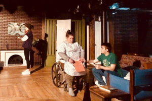 Two student actors talk while sitting while one student stands in the background in Stop Kiss at CMSV.