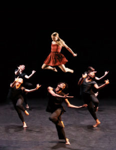 Five dancers doing dance moves in a circle.. One of them is lifted  by the others.