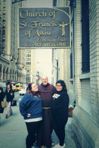 Father Chris Keenan poses with two students on a street in Manhattan next to the "Church of St. Francis of Assisi" sign.