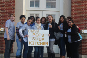 A group of leaders in service pose with a "POTS soup kitchen" sign.