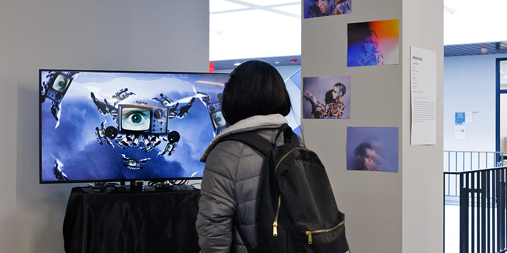 A student views a mixed media installation at the 2022 Art + VAEM Capstone Exhibit.