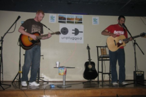 Rick Garcia '10 stands on stage with a friend; they both are playing the guitar