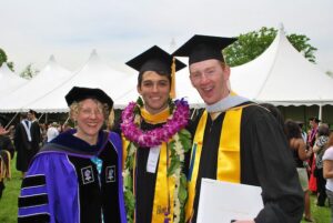 Rick Garcia '10 poses at graduation in his cap and gown with a friend and a professor