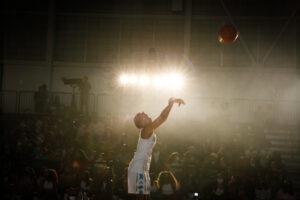 A CMSV basketball player shoots a ball against a dark background