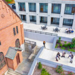A view overlooking the patio space between Founders Hall and Aquino Hall, with part of the Chapel exterior in the shot; students walk beneath.