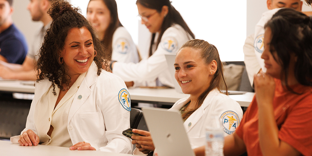A group of students in the Physician Assistant Program at the College of Mount Saint Vincent engage in conversation while smiling.