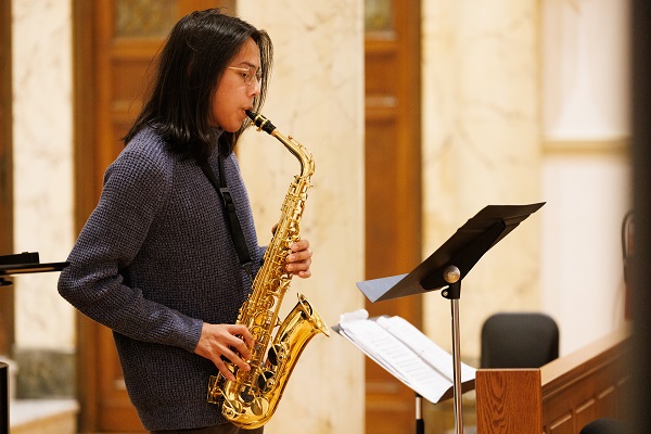 A female student plays a saxophone and looks at a music stand