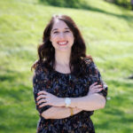 Photo of Professor Jennifer Pipitone crossing her arms and standing in front of a grassy hill