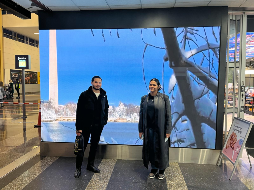 Mount Saint Vincents students pose at the Washington DC airport in front of a digital screen featuring a snowy, blue outdoor scene.