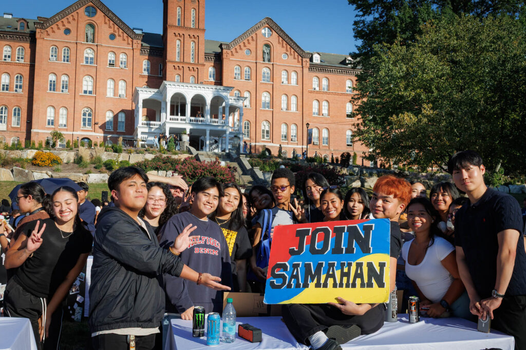 Students pose for a group photo outside the University of Mount Saint Vincent, holding a colorful “JOIN SAMAHAN” sign in front of the historic brick campus building.